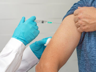 The doctor vaccinates a man. Doctor or nurse hands with syringe doing injection of vaccine to male patient. Female doctor vaccinates a man. Vaccination concept.