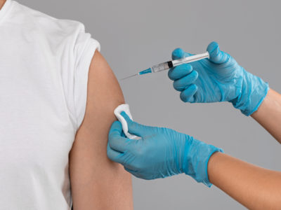 Closeup of doctor hands injecting vaccination in arm of unrecognizable man patient in clinic, grey studio background, cropped. Vaccination against COVID-19, healthcare and medical concept